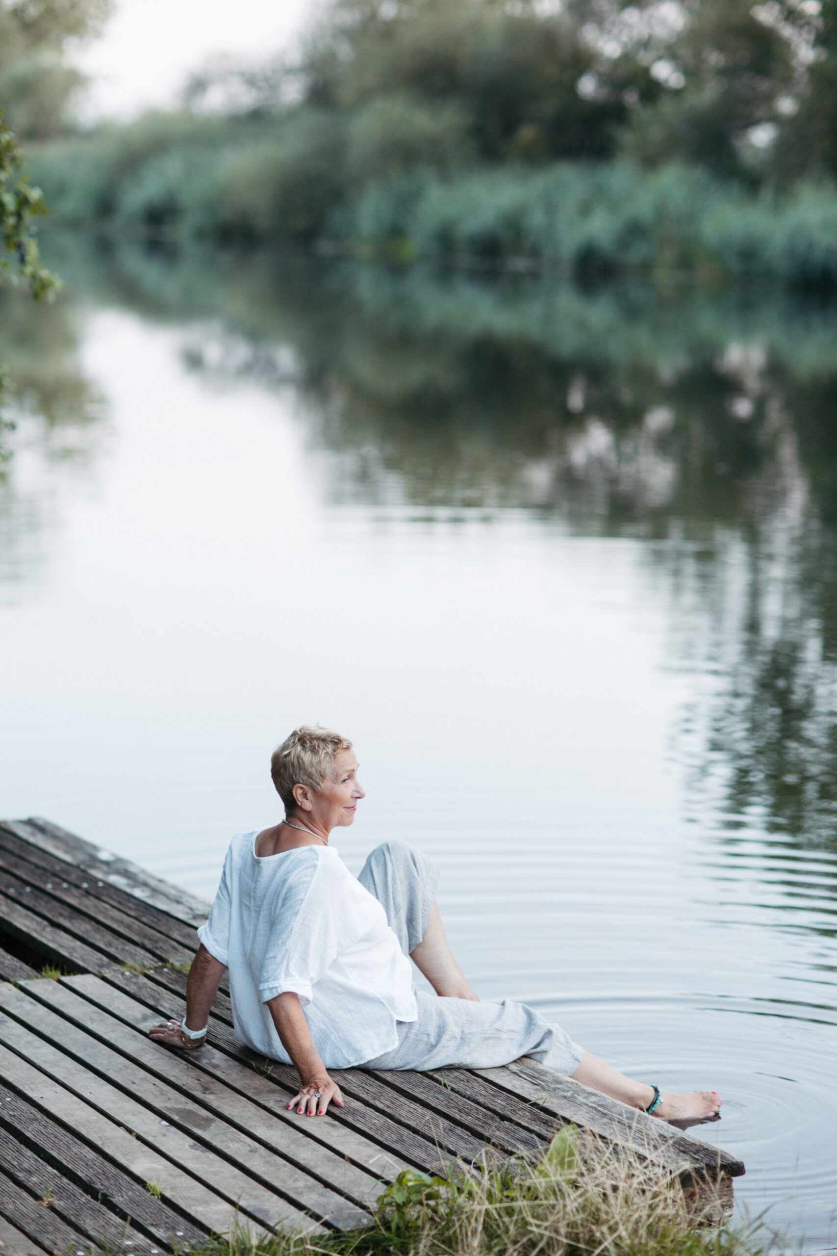 Foto von Anne - Die Bildwerkerin sitzt verträumt am Fluss und spielt mit einem Fuß im Wasser. Nähe und Verbundenheit zur Natur.