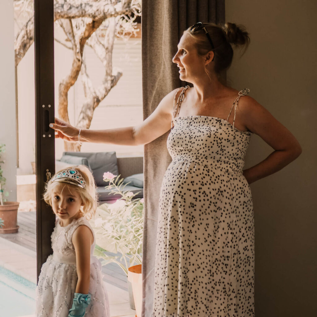Babybauch-Shooting einer schwangeren Frau mit ihrem Töchterchen am Fenster