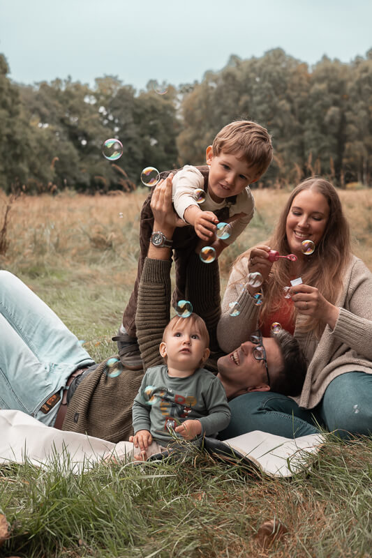 verspielte Familie bei Fotoshooting mit Seifenblasen auf der Wiese