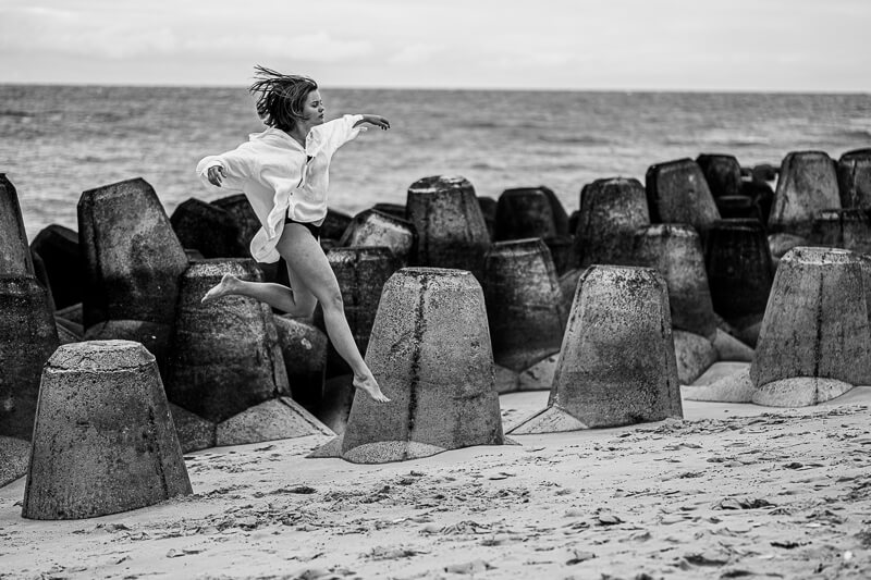 Portraitshooting am Meer - Frau springt von Betonsteinen