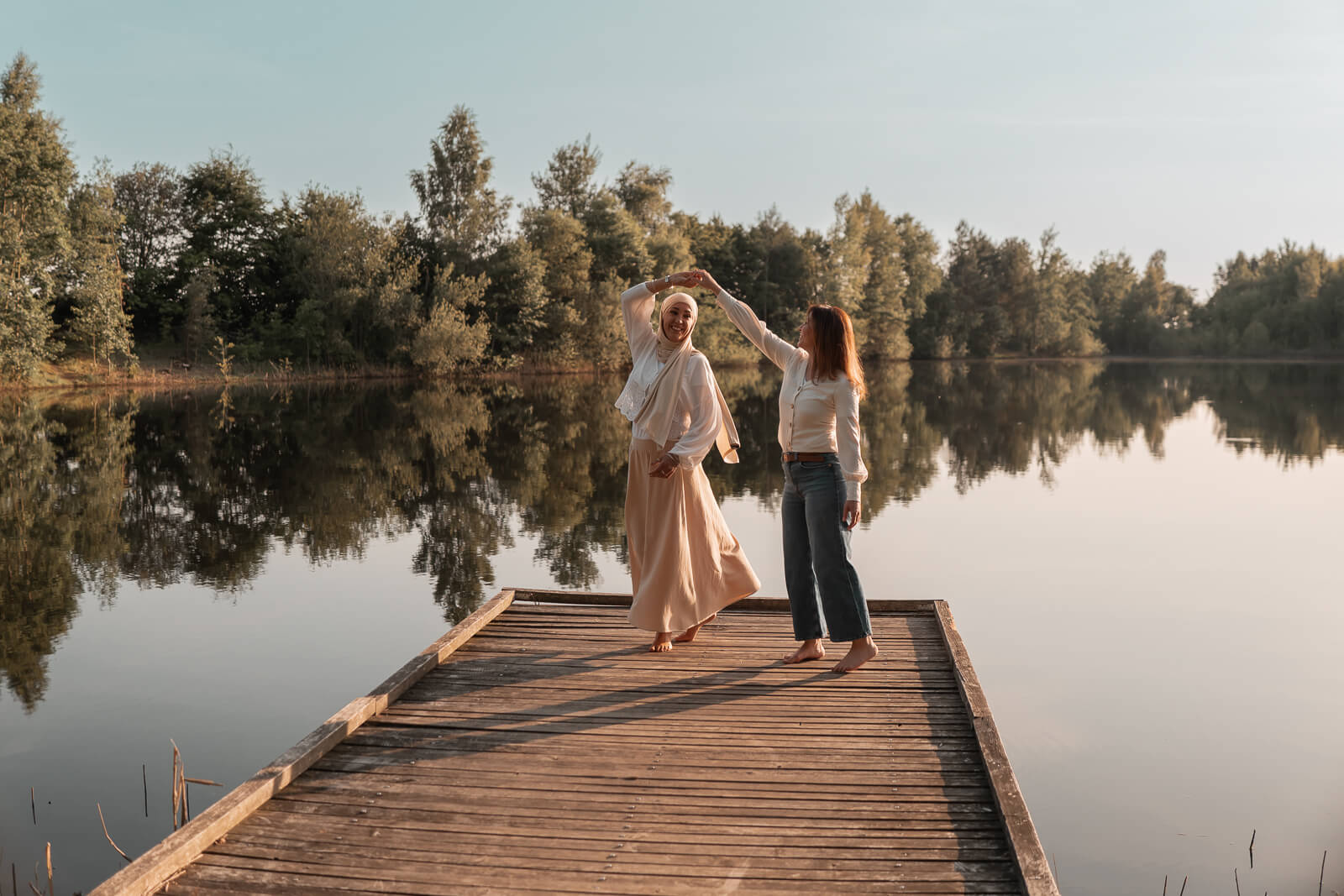 Foto von zwei besten Freundinnen die völlig frei und glücklich auf einem Steg am See tanzen