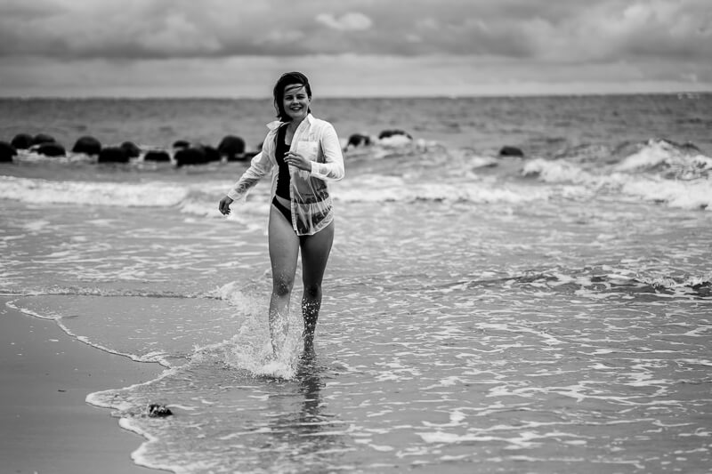 Portraitfoto am Meer - Frau läuft lachend durch aufspritzendes Wasser