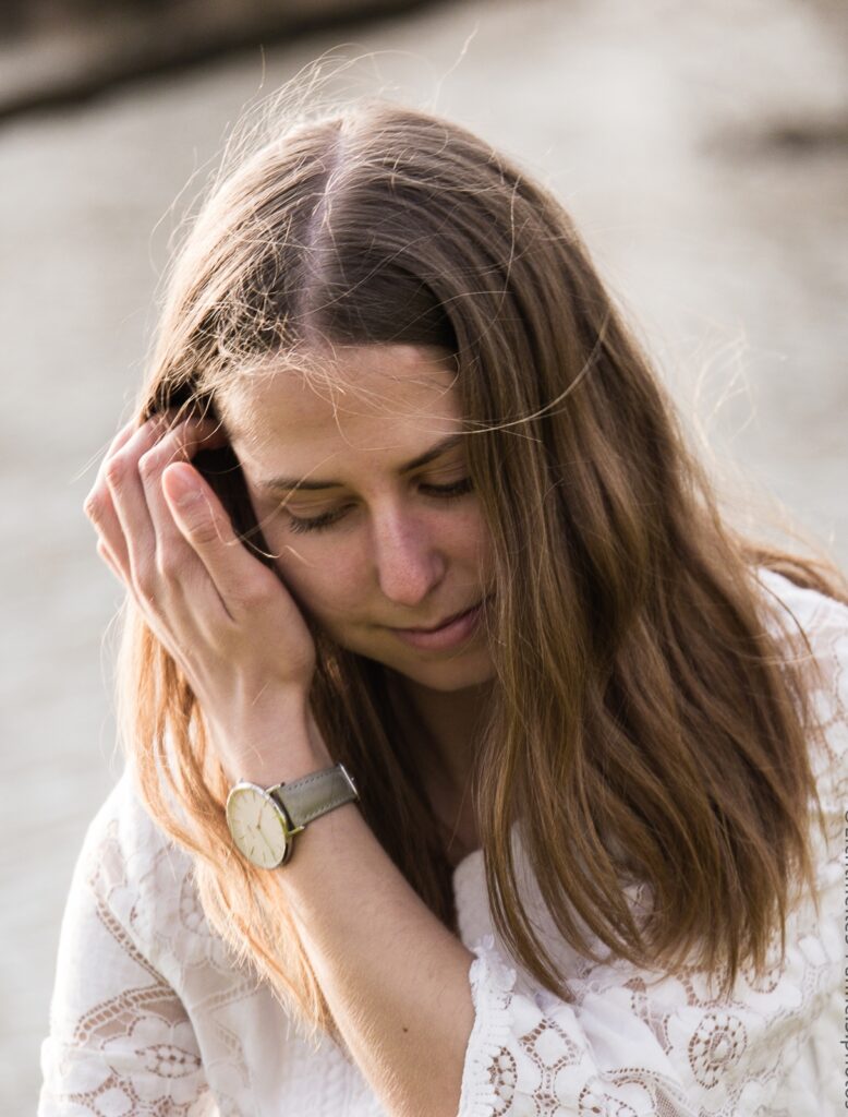 Portraitfoto Hankensbuettel einer jungen Frau, die sich, Blick nach unten die Haar wegstreicht