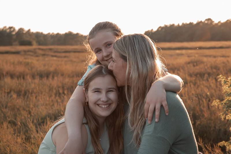 Foto von zwei Mädels zusammen mit ihrer Mutter im letzten Abendlicht auf einer Wiese