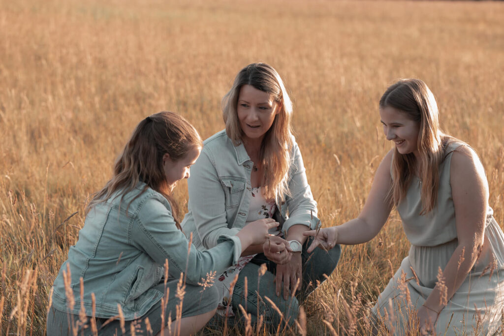 Foto einer Familie aus Mutter und 2 Töchtern beim Spielen im hohen Gras