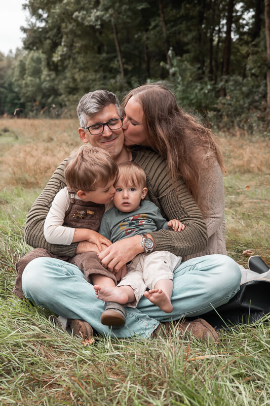 Foto einer Familie auf einer Wiese sitzend und ungezwungen schmusend