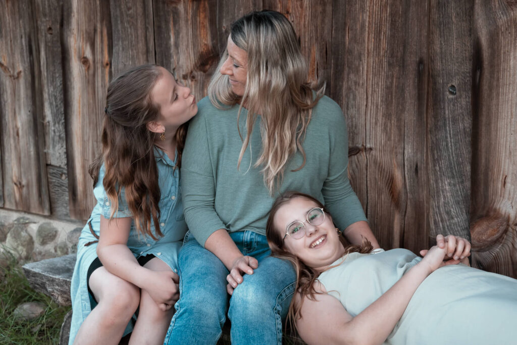 kleine Familie fotografiert vor einer Holzwand auf einer Bank sitzend.