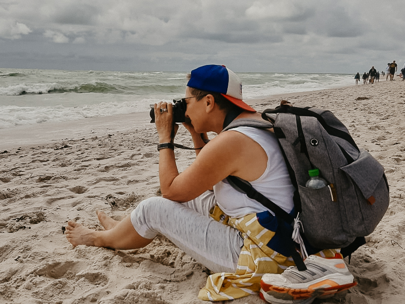 Fotografin Anne. Die Bildwerkerin mit Kamera und Rucksack beim Fotografieren. Nähe zum Meer