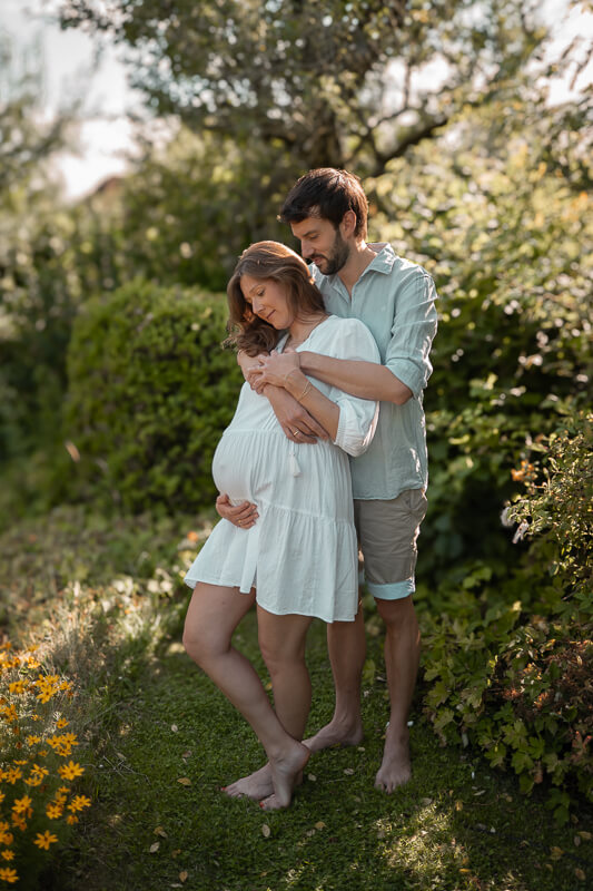 Foto eines Paares. Sie mit einem runden Babybauch im weißen Sommerkleid