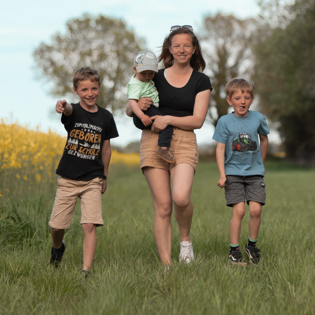 Mama mit 3 Jungs am Rapsfeld gehen auf die Kamera zu 